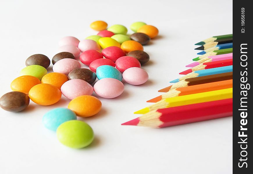 Color pencils and multi-colored sweets on a white background