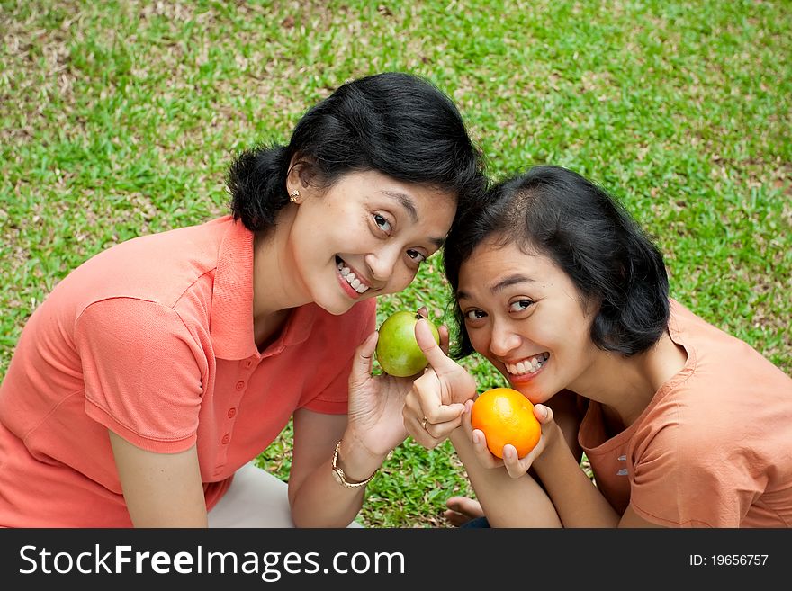 Two happy asian ethnic sisters showing their love of tropical fruits. Two happy asian ethnic sisters showing their love of tropical fruits