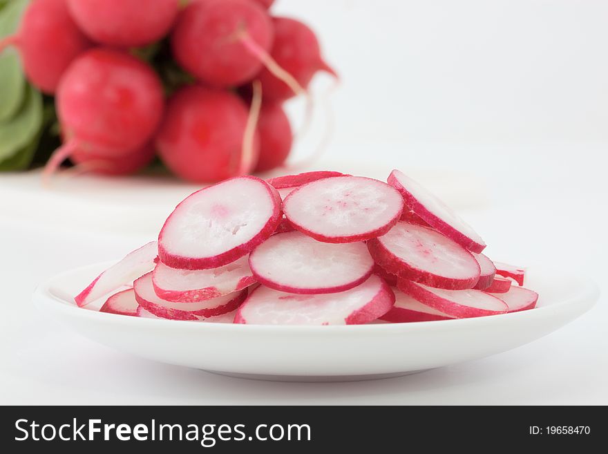 Sliced radishes in a plate against a radish bunch not in focus. Sliced radishes in a plate against a radish bunch not in focus.