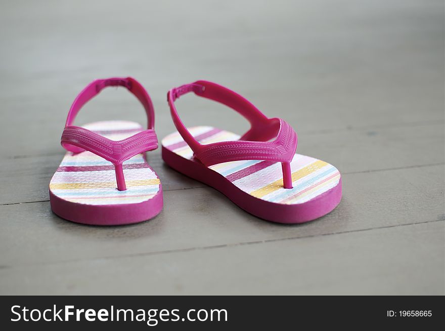 A little girl's thong sandals sit on a wooden floor. A little girl's thong sandals sit on a wooden floor.
