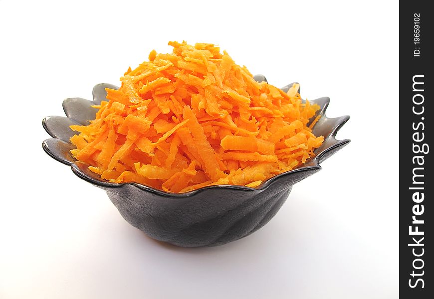 Grated orange carrot in a black plate on a white background. Ð¢ÐµÑ€Ñ‚Ð°Ñ Ð¼Ð¾Ñ€ÐºÐ¾Ð²ÑŒ Ð² Ñ‚Ð°Ñ€ÐµÐ»ÐºÐµ