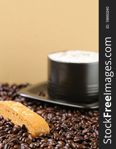 A creamy cappuccino in a black cup with a caramel biscotti on a bed of coffee beans with a shallow DOF. A creamy cappuccino in a black cup with a caramel biscotti on a bed of coffee beans with a shallow DOF.