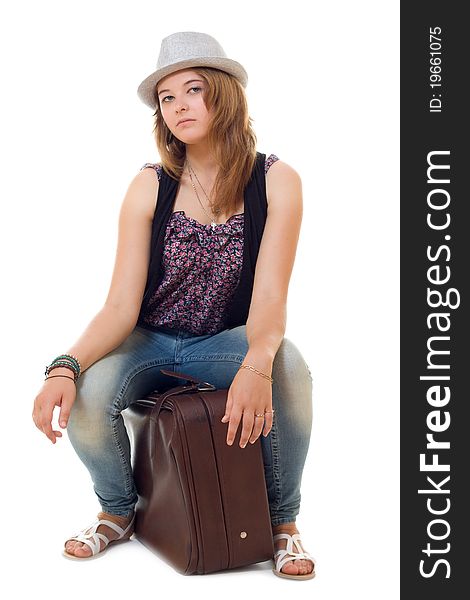 Attractive girl in hat is sitting on vintage suitcase. Studio shot isolated over white background
