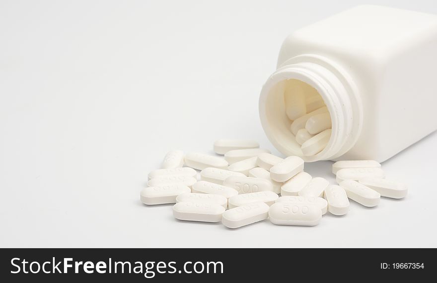 Pills scattered from vials against white background