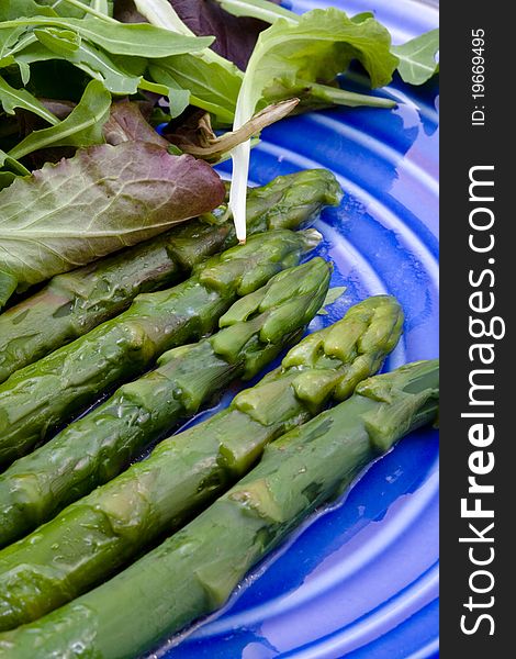 Boiled green asparagus with salad mix on blue plate