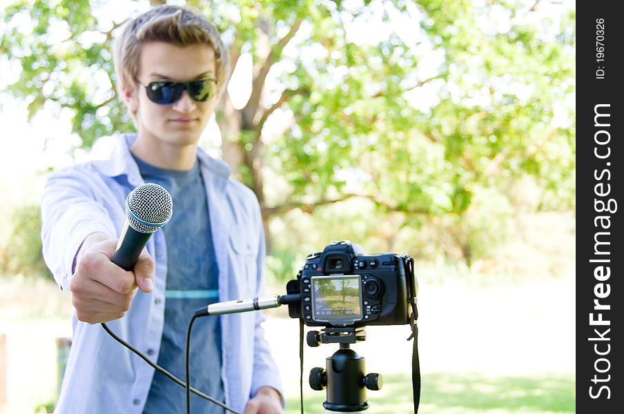 Young man holding a microphone connected to a D SLR. Focus on the microphone only. Young man holding a microphone connected to a D SLR. Focus on the microphone only.