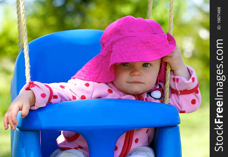 Infantâ€™s sitting happily in swing with floppy bright colored sun hat. Infantâ€™s sitting happily in swing with floppy bright colored sun hat