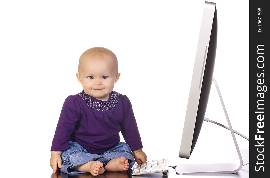 Infant baby girl sitting up looking playing with a desktop computer screen and keyboard. Infant baby girl sitting up looking playing with a desktop computer screen and keyboard.