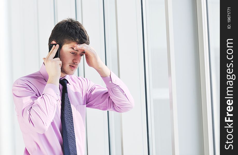 Young business man talk by cellphone over bright window in big hall