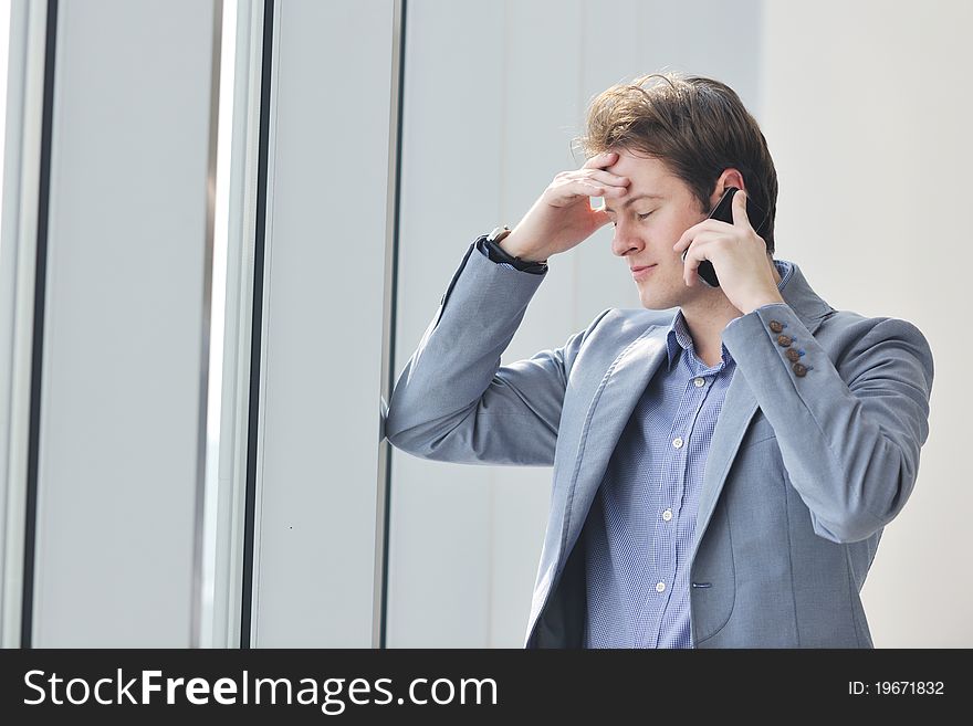 Young business man talk by cellphone over bright window in big hall