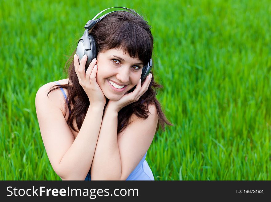 Happy smiley girl with the headphones on a grass