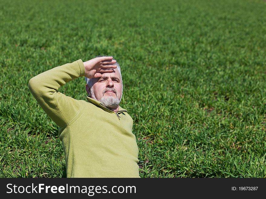 Old man sitting on a green field. Old man sitting on a green field