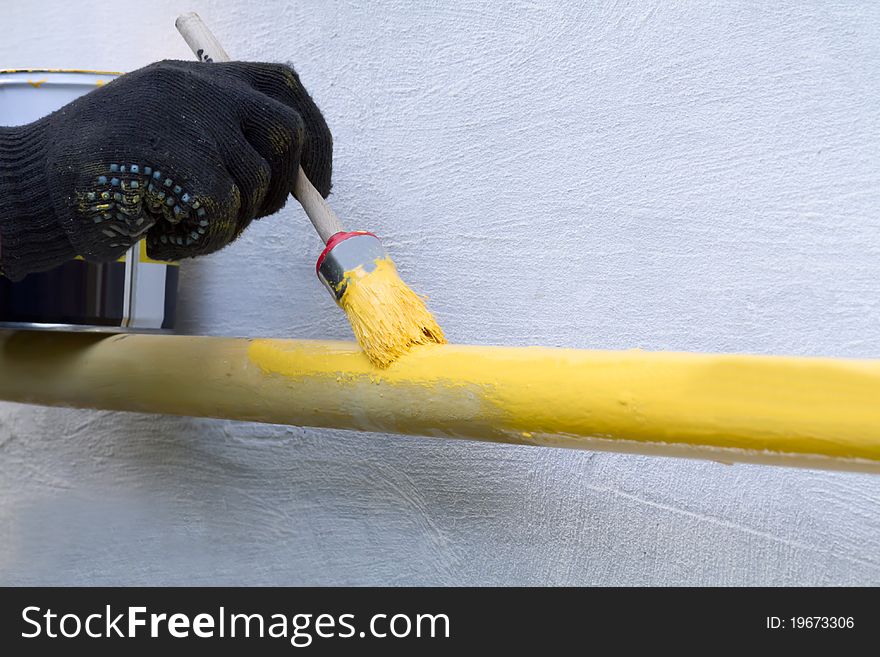 Painting the pipe with a brush with yellow paint. Painting the pipe with a brush with yellow paint