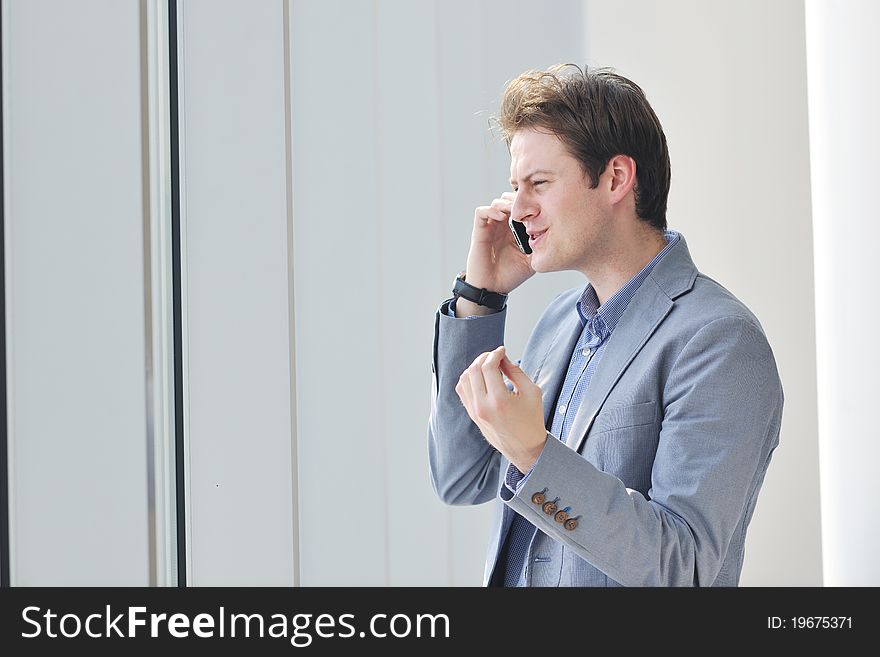 Young business man talk by cellphone over bright window in big hall