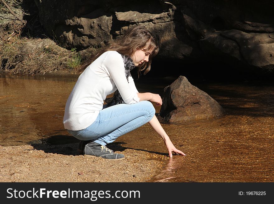 Young woman gently dipping her hand into the cold shallow water. Young woman gently dipping her hand into the cold shallow water