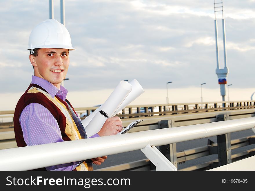 Industrial theme: architect, on a workplace, in a warm winter jacket and a helmet, has control over a tablet. Industrial theme: architect, on a workplace, in a warm winter jacket and a helmet, has control over a tablet.