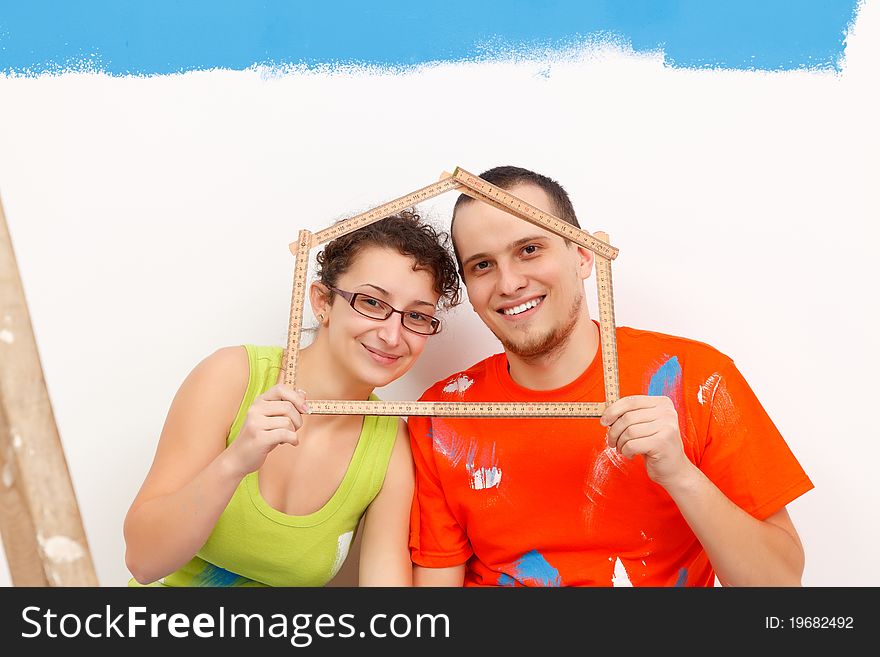 Happy couple with a folding rule in their hands in form of a house. Happy couple with a folding rule in their hands in form of a house