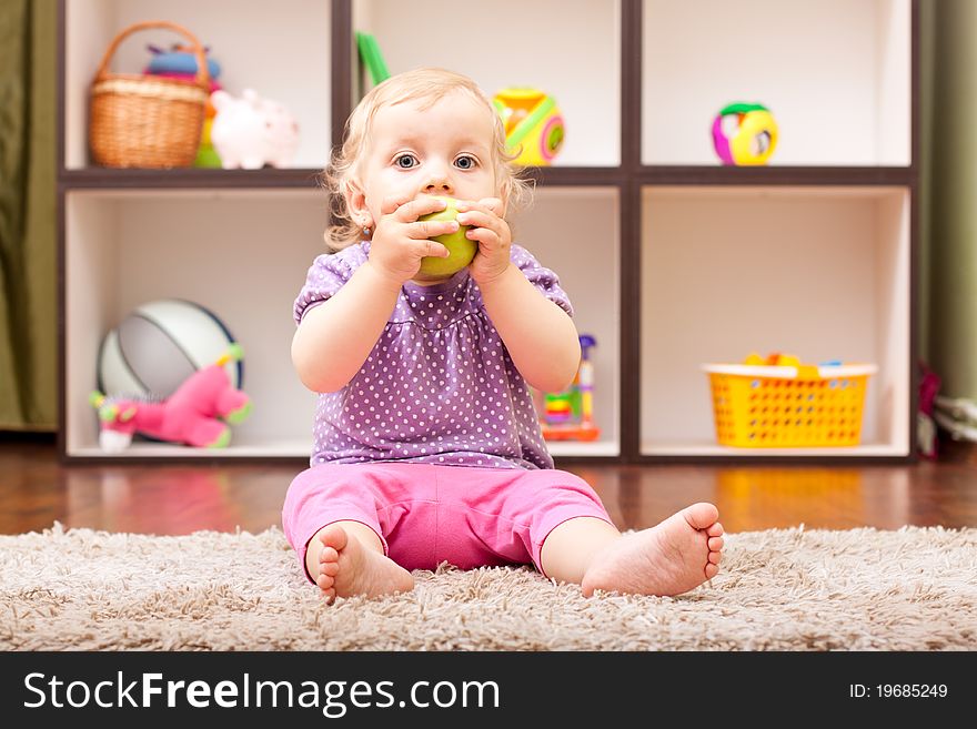 Cute baby girl eating a green apple in her room. Cute baby girl eating a green apple in her room