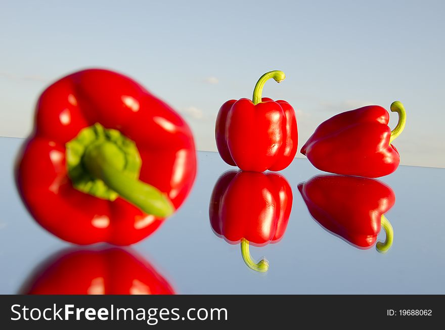 Three red peppers on mirror and sky background