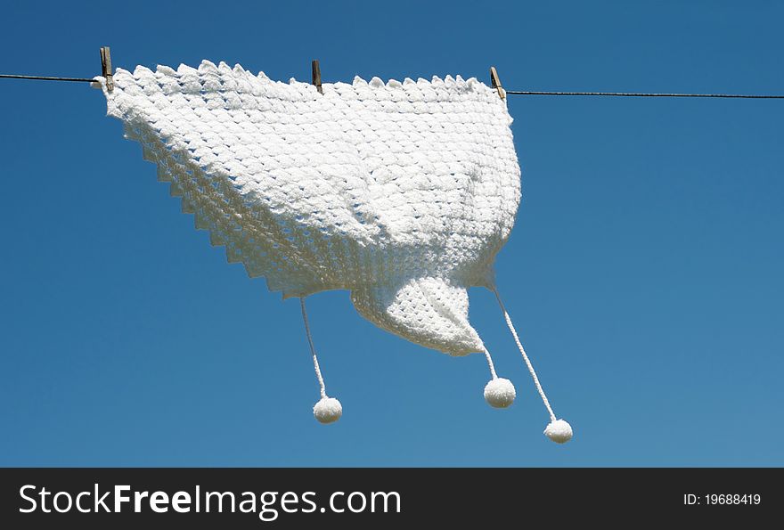 A hand knitted baby shawl hangs drying on a clothesline against a brilliant blue sky with copy space. A hand knitted baby shawl hangs drying on a clothesline against a brilliant blue sky with copy space.