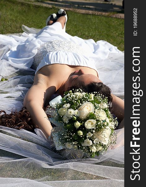 The bride with a bouquet lying on a grass. The bride with a bouquet lying on a grass