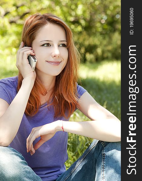 Beautiful redhead girl with mobile phone at the park in summer time.