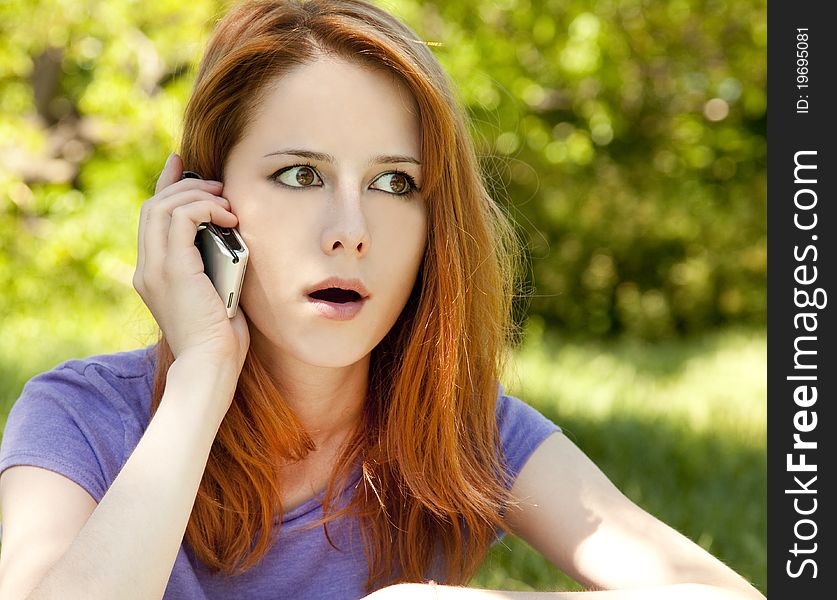 Surprised redhead girl with mobile phone at the park in summer time.