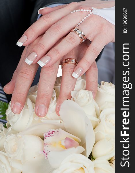 Photo of two tender hands of the groom and the bride with wedding rings and bouquet of white roses close up. Photo of two tender hands of the groom and the bride with wedding rings and bouquet of white roses close up