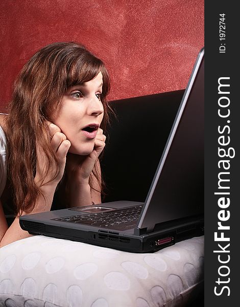 A young woman looking shocked in front of her laptop on the couch. A young woman looking shocked in front of her laptop on the couch.