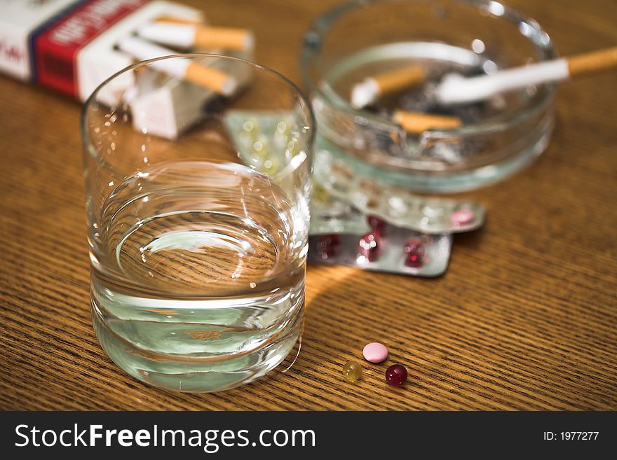 Glass with water, cigarettes, tablets and ashtray on a table, (studio). Glass with water, cigarettes, tablets and ashtray on a table, (studio).