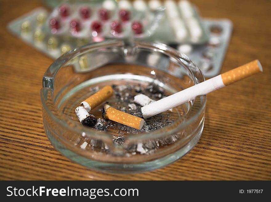 Cigarette, tablets and ashtray on a table, (studio, halogen light). Cigarette, tablets and ashtray on a table, (studio, halogen light).