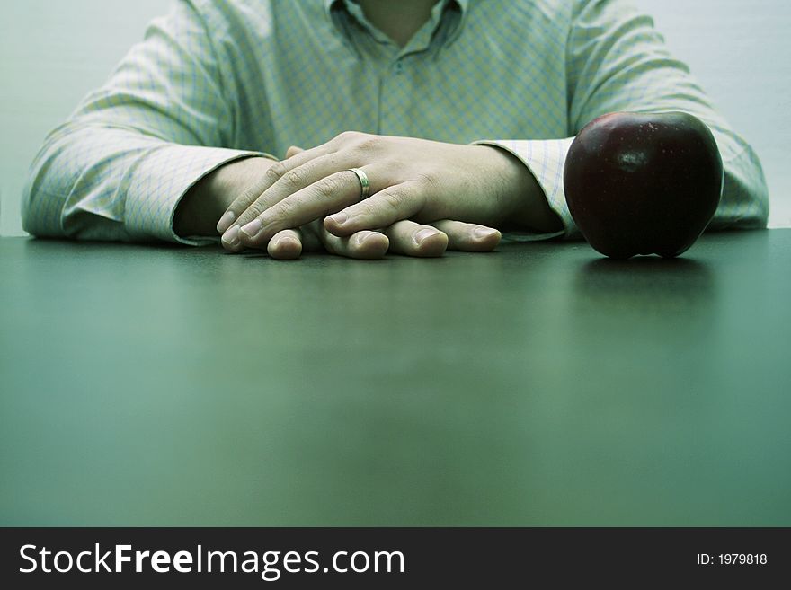 Male hands on a brown table and an apple. Male hands on a brown table and an apple