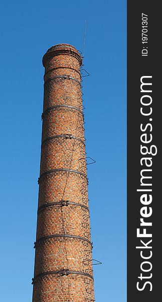 The old brick chimney with a ladder against the blue sky