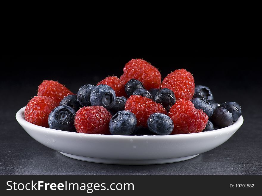 Plate of fresh blueberries and raspberries on black background