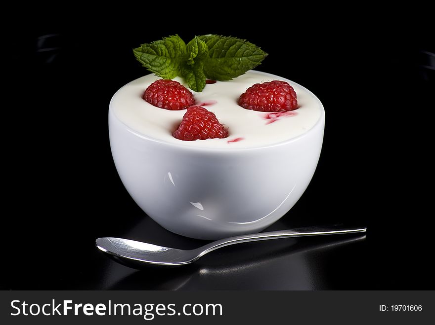 Bowl of yogurt with raspberries and mint on black background