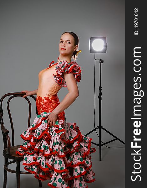 Young woman near the chair dancing flamenco on grey background. Young woman near the chair dancing flamenco on grey background