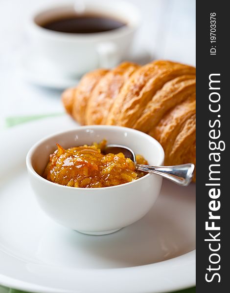 Orange jam,croissant and a cup of black coffee in background. Orange jam,croissant and a cup of black coffee in background