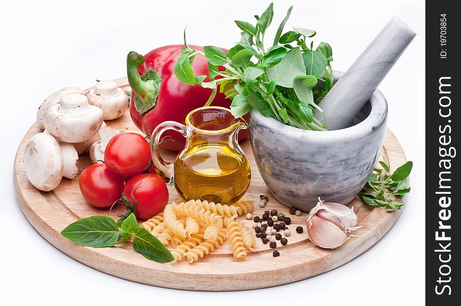 Mortar with pestle, basil herbs, olive oil and vegetables. Products are on a round desk. Mortar with pestle, basil herbs, olive oil and vegetables. Products are on a round desk.