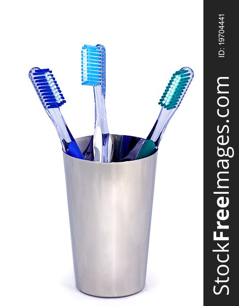 Three toothbrushes in a metal cup on white background