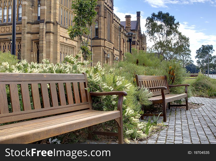 Two wooden benches with flowers in front of old sandstone building. Two wooden benches with flowers in front of old sandstone building