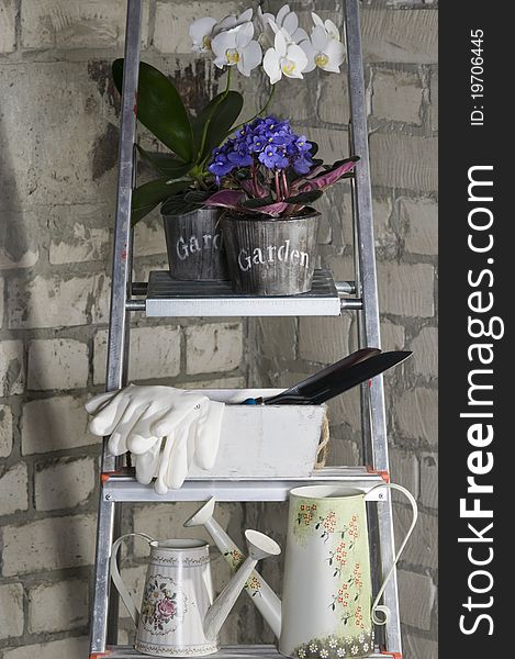 Gardening tools and flowers on a metal stepladder over grey brick wall. Gardening tools and flowers on a metal stepladder over grey brick wall.