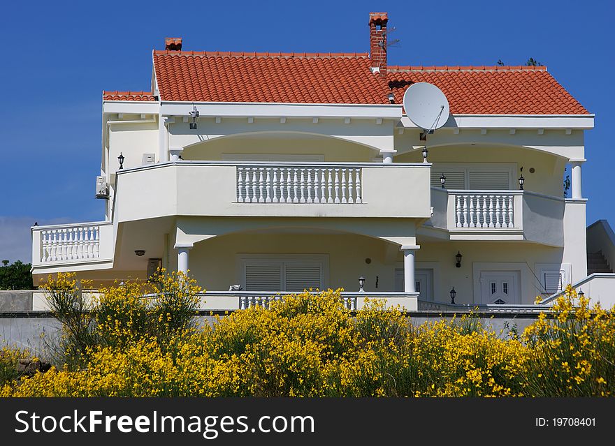 White villa is decorated with yellow flowers in front of it. In the background is blue blue sky. White villa is decorated with yellow flowers in front of it. In the background is blue blue sky.