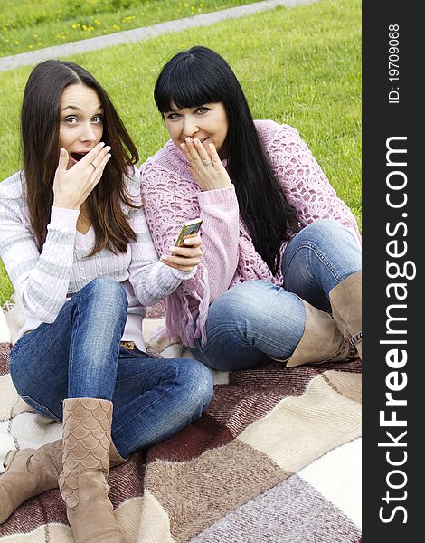 Attractive mother and daughter teen in the park watching the phone expressed surprise and joy. Attractive mother and daughter teen in the park watching the phone expressed surprise and joy