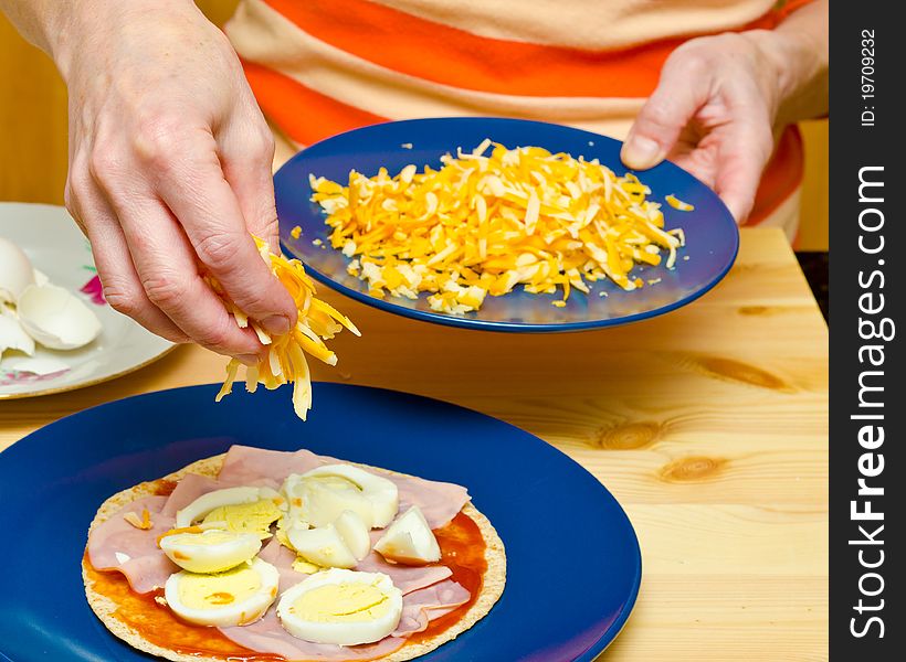 Closeup hands making pizza at kitchen. Pouring cheese on pizza. Closeup hands making pizza at kitchen. Pouring cheese on pizza.