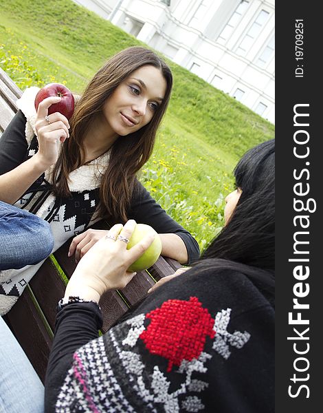 Mother and daughter in a park sitting on a wooden bench eating apples