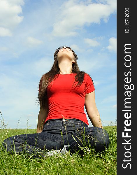 Young girl siting on summer meadow and looking up, blue sky