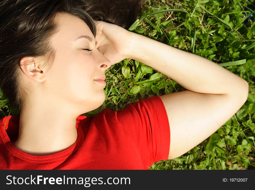 Closeup of young brunette girl lying on summer meadow and smiling, closed eyes