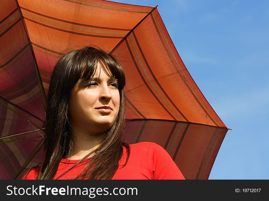 Young brunette girl holding red umbrella, blue sky