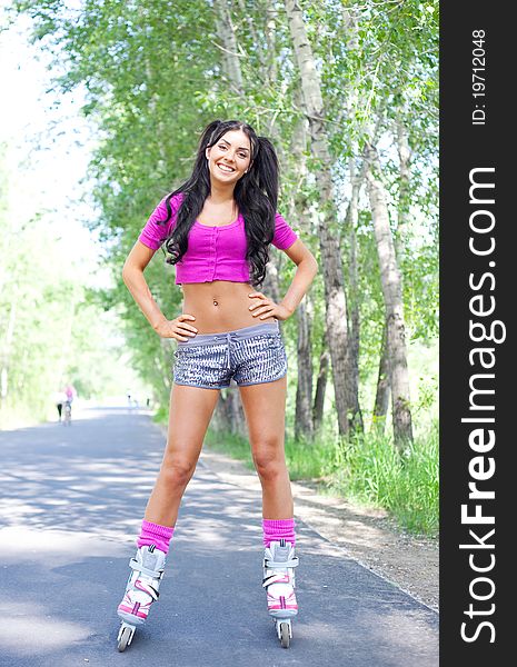 Happy young brunette woman on roller skates in the park