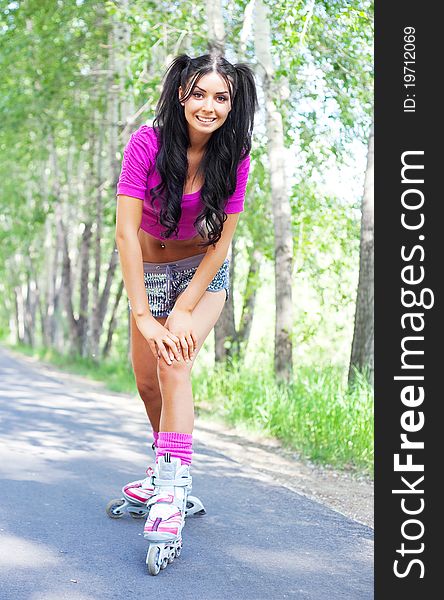 Happy young brunette woman on roller skates in the park